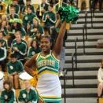 Two cheerleaders in 罗斯福 school colors of green and gold lead a crowd in cheer